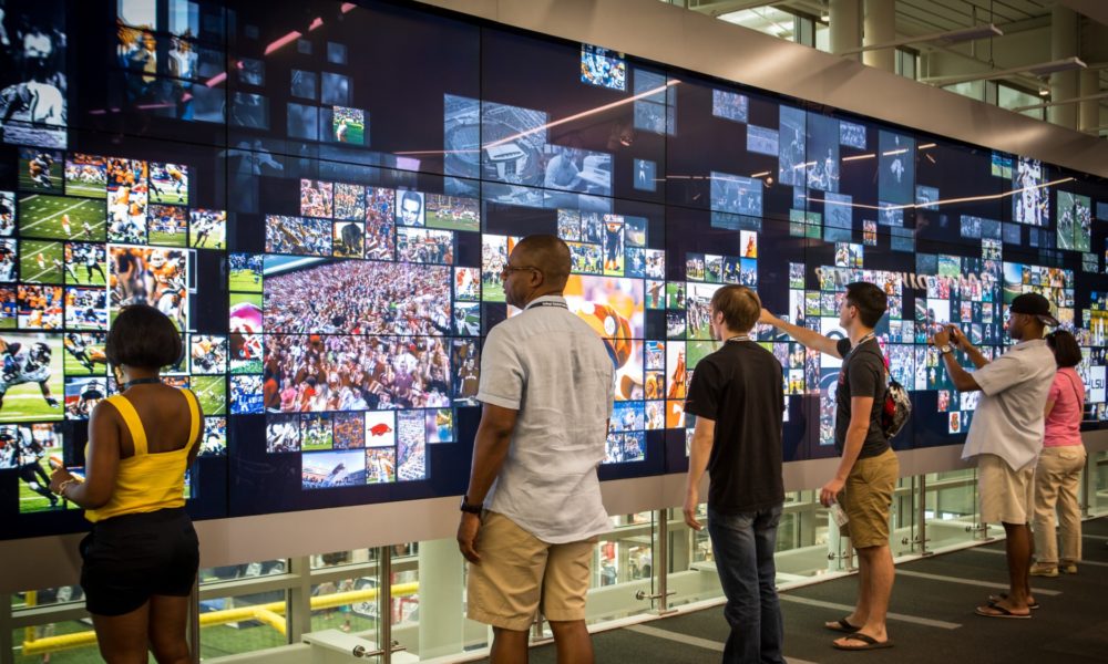 Des visiteurs interagissent avec l’écran tactile géant du College Football Hall of Fame